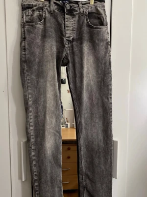 Grå tvättade raka jeans - Säljer ett par grå tvättade jeans med raka ben och klassisk femficksmodell. Jeansen har en avslappnad passform och tydliga sömmar. Midjan mäter 39 cm och längden är 110 cm. Perfekta för en cool och avslappnad stil.