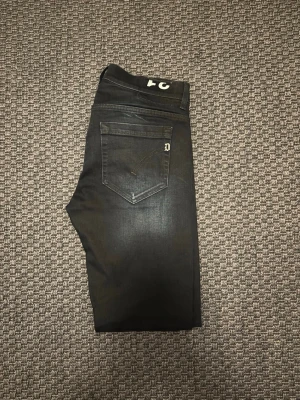 Dondup jeans - Säljer ett par svarta skinny jeans med stretch och klassisk femficksdesign. Jeansen har en diskret tvättad look och smala ben. Passar perfekt till en avslappnad eller trendig stil. Materialet känns mjukt och följsamt.