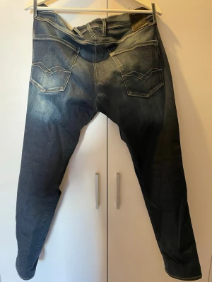 Mörkblåa replay anbass  - Snygga mörkblå jeans med ljusa kontrastsömmar och klassiska fem fickor. Jeansen har en lätt tvättad look och raka ben. Bakfickorna har dekorativa sömmar som ger extra stilpoäng. Perfekta för en avslappnad och trendig outfit.