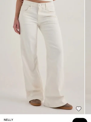 Vida vita jeans från Nelly🤍 - Säljer ett par snygga vita jeans från Nelly med hög midja och vida ben. Jeansen har klassisk femficksmodell och stängs med dragkedja och knapp. Jag är 173 cm lång och säljer på grund av att de är lite för korta för mig! I väldigt gott skick! Nypris:699 