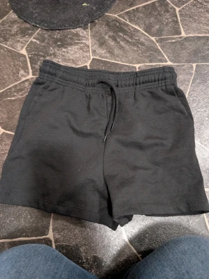 Svarta shorts med snörning XS - Ett par svarta shorts i mjukt material med elastisk midja och snörning framtill. Perfekta för avslappnade dagar eller träning. Klassisk och enkel design som passar till det mesta.