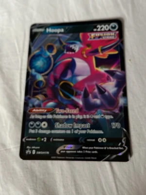 Pokémonkort Hoopa V - Säljer ett Pokémonkort med motivet Hoopa V. Kortet har en färgstark design med lila, rosa och blå nyanser samt holografiska detaljer. Text och symboler på engelska. Perfekt för samlare eller Pokémonfans.