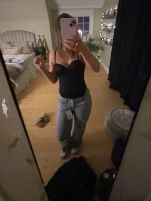Svart snygg body - Snygg svart body med bygelkupor och smala axelband. Materialet är glansigt och stretchigt, vilket ger en tight och bekväm passform. Perfekt att styla under jeans eller kjol för en trendig look.