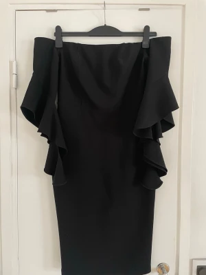 Svart offshoulder klänning  - Snygg svart offshoulder klänning med stora volangdetaljer längs ärmarna. Klänningen har en figurnära passform och slutar strax under knät. Är i strl S men skulle säga att det mer är en M