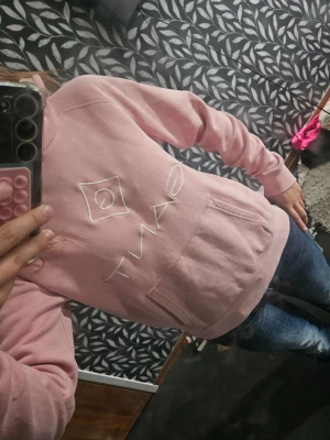 Rosa hoodie från Gant med logga - Säljer en ljusrosa hoodie från Gant med stor vit broderad logga på bröstet och klassisk känguruficka framtill. Hoodien har ribbade muddar vid ärmslut och nederkant samt en mjuk, bekväm passform. Perfekt för dig som gillar stilrena och sköna plagg. Str 159 164 men passar som en xs