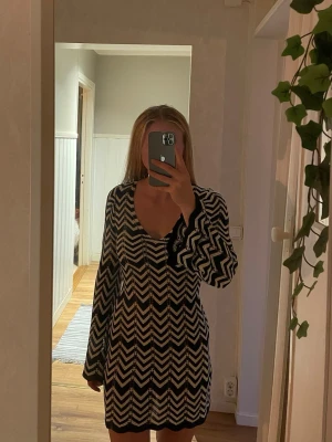 Svartvit stickad kortklänning - Säljer en svartvit stickad kortklänning med zigzag-mönster. Klänningen har långärmade ärmar, v-ringad hals och en figurnära passform. Aldrig använd!