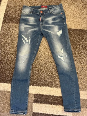 Blå slitna skinny jeans - Säljer ett par blå skinny jeans med slitningar och ljusa tvättade partier. Jeansen har fem fickor, knappgylf och smal passform. Materialet är klassisk denim med stretch för extra komfort. Perfekta för en trendig och avslappnad look.