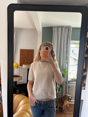 Beige kortärmad stickad tröja - Säljer en enkel och stilren beige stickad tröja med korta ärmar och rund hals. Tröjan har en rak passform och är perfekt att matcha med jeans för en avslappnad look. Materialet är mjukt och bekvämt.