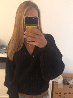 Svart omlottstickad tröja - Säljer en svart stickad omlott-tröja med breda ärmar och knytband i midjan. Tröjan har en djup v-ringning och är ribbstickad.🥰