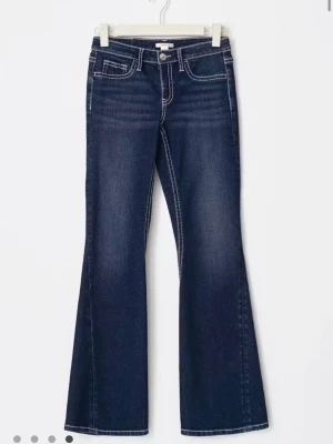 Iconic twisted jeans - Snygga mörkblå bootcut jeans med vita kontrastsömmar och utsvängda ben. Jeansen har klassiska fem fickor och dekorativa sömmar på bakfickorna. Tillverkade i stretchig denim för skön passform. Storlek 164 passar som S/XS, Endast testad 🥰