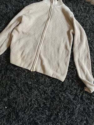 Beige ribbad ziptröja - Säljer en beige ribbad ziptröja med lång ärm och hög krage. Tröjan har en rak passform och dragkedja framtill. Perfekt för lager-på-lager och enkel att matcha med olika outfits.