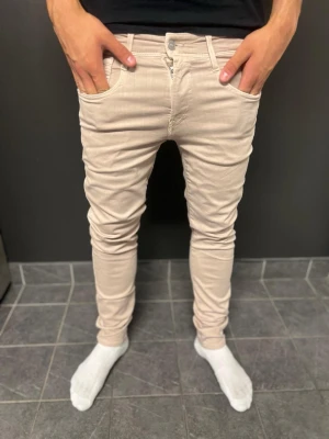 Replay jenas  - Snygga beige slim jeans från Replay med klassisk femficksmodell och smal passform. Jeansen har en ljus ton och är tillverkade i ett stretchigt material som sitter tajt längs benen. Perfekta för dig som gillar en modern och stilren look.