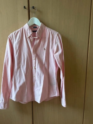 Ljusrosa skjorta från Ralph Lauren - Tjena säljer nu denna riktigt feta rosa Ralph skjortan. Den är riktigt fräsch och kommer passa riktigt bra nu inför sommaren. Den är i storlek xs och skicket är 8/10 den är använd och har ett litet hål som ni ser på bild 5 men absolut inget man tänker på och detta pris är sjukt bra, då dessa skjortor är sjukt svåra att få tag i för bra pris och säljer fort slut. Om de är något är de bara att skriva. Själv klart äkta! Å nej de är inte dam de är unisex!