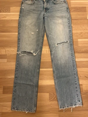 Ljusblå raka jeans med slitningar - Säljer ett par ljusblå jeans från zara med raka ben med hål och slitningar samt fransiga benslut. Midwaist. 