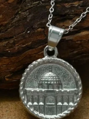 Palestine Silverfärgat halsband med kupolberlock - Snyggt halsband i silverfärg med en rund berlock som har ett detaljerat motiv av en byggnad med kupol, inramad av ett tvinnat mönster. Kedjan är tunn och stilren, perfekt för dig som gillar unika smycken med arkitektoniska detaljer.