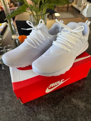 Nike Air helvita sneakers - Snygga helvita Nike Air sneakers med mesh-ovandel och klassisk swoosh på sidan. Skorna har vita snören, plastdetaljer vid snörningen och en bekväm, vadderad insida. Perfekta för dig som gillar stilrena och sportiga sneakers.