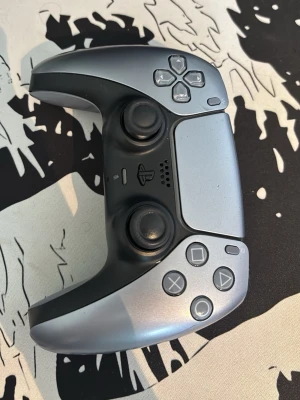 Silverfärgad PS5 DualSense handkontroll - Snygg och modern handkontroll till PlayStation 5 i metallic silver och svart. Ergonomisk design med två analoga spakar, klassiska PlayStation-knappar och touchpad. Tillverkad i plast med en matt finish som ger ett stilrent intryck.