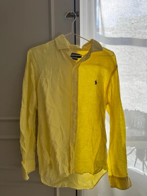 Gul linneskjorta från Polo Ralph Lauren - Snygg gul skjorta i linne från Polo Ralph Lauren med klassisk krage och lång ärm. Slim fit-modell med knappar framtill och den ikoniska broderade loggan på bröstet. Perfekt för dig som vill ha en fräsch och stilren look.
