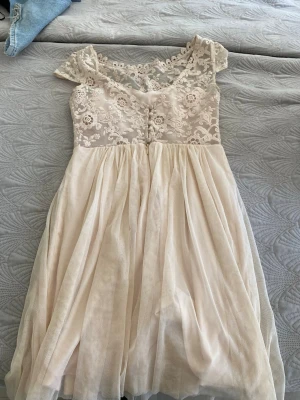 Klänning med blommönster/spets - Underbar flowig klänning i en pastelbeige färg. Med spets från midjan och uppåt (finns ett skyddande lager under). Båt ringad. Bakifrån finns det både en dragkedja och knappar men annars är den rätt så låg i ryggen. Står ingen lapp med storlek men skulle gissa på att den är storlek S. 