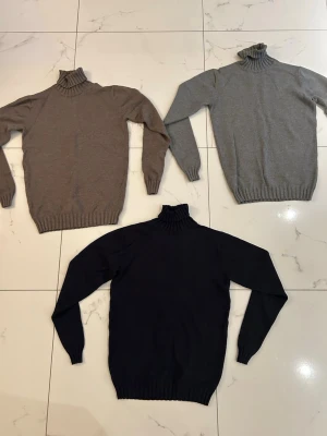 Tre polotröjor i stickat material - Säljer tre stickade polotröjor i olika färger: mörkblå, ljusgrå och beige. Alla har lång ärm, ribbstickade muddar och hög polokrage. Perfekta för lager på lager och riktigt sköna under kalla dagar. 