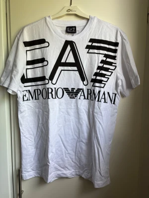 T-shirt med tryck på. - Vit t-shirt med svart tryck på. Band där lapp suttit finns kvar. Den är aldrig använd, bara legat i garderob.