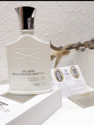 Creed Silver Mountain Water parfym - Exklusiv parfym från Creed, Silver Mountain Water, i en elegant vit flaska med silverfärgad spraykork. Flaskan har en stilren och lyxig design med präglad logotyp och text. Perfekt för dig som gillar fräscha och unika dofter.