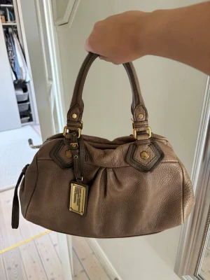 Beige Marc Jacobs väska - Säljer min så fina Marc Jacobs väska som är använd försiktigt, köpte den på plick men har knappt använt den sedan. Band medföljer!❤️ lite slitningar på väskan men det ser mest snyggt ut och inget man tänker på