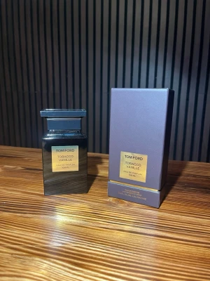 Tom Ford Tobacco Vanille EdP 100 ml - Tom Ford Tobacco Vanille Eau de Parfum i en elegant mörkbrun glasflaska med guldlabel. Doften kombinerar varma toner av tobak och vanilj för en lyxig och djup parfymupplevelse. Flaskan har en stilren, fyrkantig form och levereras med matchande förpackning. Helt oanvänd skriv vid frågor! 