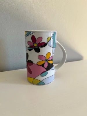 Mugg / Kopp med färgglatt blommönster - Söt och färgglad mugg med ett dekorativt blommönster i härliga färger! Har handtag. Storlek: Höjd: ca 12 cm. Diameter: ca 7 cm. Säljs i bra skick! Det finns några mindre nagg på muggen här och där. Se gärna bilder för att själv bedöma och avgöra dess skick! Kika gärna in på mina andra annonser, jag säljer just nu flera muggar och glas. Hör gärna av dig vid frågor och intresse!
