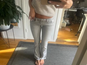 Gråa jeans  - Säljer ett par ljusgrå bootcut jeans med klassisk femficksmodell och låg midja. Jeansen har en snygg tvätt och raka ben som går ut lite nedtill. Perfekta för en avslappnad och trendig look.
