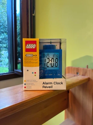 Blå digital LEGO väckarklocka - Säljer en blå digital väckarklocka från LEGO med stor LCD-display och tydliga knappar framtill. Klockan har en klassisk LEGO-klossdesign och visar både tid och datum. Perfekt för dig som gillar LEGO och vill ha en unik accessoar på nattduksbordet.