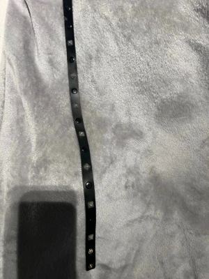Svart läderarmband/halsband med nitar - Snyggt svart armband i läder med silverfärgade pyramidformade nitar längs hela bandet. Armbandet har tryckknappar för enkel justering och en cool, edgy look som passar till många stilar.