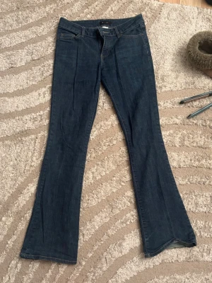 Mörkblå bootcut jeans - Säljer ett par mörkblå bootcut jeans med klassisk femficksdesign och låg midja. Jeansen har utsvängda ben och är tillverkade i ett denimtyg med lite stretch. 