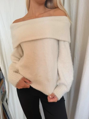 cremevit fluffig stickad tröja - Trendig cremevit stickad tröja med bred off shoulder-krage och långa ärmar. Tröjan har en mjuk, fluffig känsla och ribbade muddar vid ärmslut och nederkant. Perfekt för dig som vill ha en stilren och mysig look.