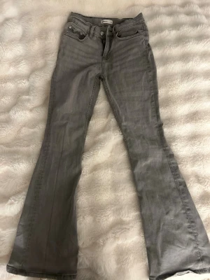 Grå bootcut jeans från Gina tricot - Snygga grå jeans från Gina i storlek 34. Modellen har bootcut-ben och klassisk femficksdesign. Jeansen är tillverkade i ett mjukt denimtyg som ger en bekväm passform och cool look. Perfekta till sneakers eller boots.