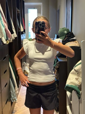 Vit topp med volangärmar - Säljer en söt vit topp med ribbad struktur och volangprydda korta ärmar i spets. Toppen har en croppad passform och rund halsringning. Perfekt för dig som gillar en feminin och trendig stil.
