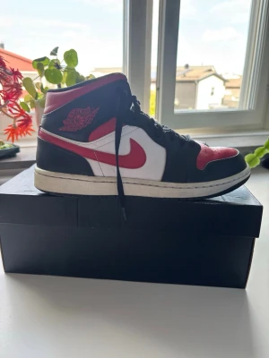 Nike Air Jordan 1 mid fire red - Säljer ett par klassiska Nike Air Jordan 1 mid sneakers i svart, rött och vitt. Skorna har den ikoniska swoosh-loggan på sidan och Air Jordan-vingen på ankeln. Ovandelen är i läder med perforerad tåbox och svart snörning. Perfekt för dig som gillar streetwear. Samt lite tecken på användning vid tårna samt sulan 