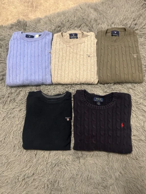 Kabelstickade tröjor från Gant & Polo Ralph Lauren - Fem kabelstickade tröjor i olika färger: ljusblå, grå, olivgrön och marinblå. Fyra av tröjorna är från Gant och en marinblå från Polo Ralph Lauren. Alla har rund hals och diskret logga broderad på bröstet. Perfekta för lager på lager och snygg preppy stil. Vid köp av en tröja 150kr, vid köp av flera blir styck priset 100kr. Kontakta mig med info om vad du är intresserad av så fixar jag till det rätta priset. Vid behov av fler bilder kontakta mig🫶🫶