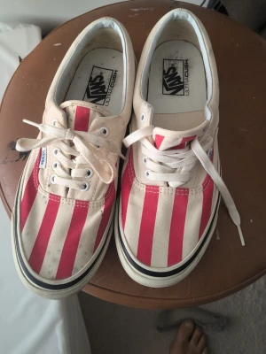 Vans randiga låga sneakers - Säljer ett par klassiska Vans sneakers med röda och vita vertikala ränder. Skorna är låga med vit sula och har vita snören. Ovandelen är i canvas och sulan är i gummi. Perfekta för dig som vill sticka ut med en retroinspirerad look.