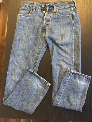 Blå raka jeans med hög midja - Levis jeans i modellen 501 de är Klassiska blå jeans med hög midja och knappgylf. Jeansen har fem fickor och kontrastsömmar. Tillverkade i slitstark denim med en ljus tvätt och vintagekänsla. Perfekta för en avslappnad och trendig stil. Storlek 29/32