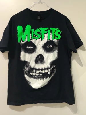 Svart Misfits t-shirt  - Säljer en svart t-shirt med stort Misfits-tryck i grönt och vitt på framsidan. T-shirten har korta ärmar och är gjord i mjuk bomull. Perfekt för dig som gillar bandmerch och vill sticka ut med en ikonisk design.