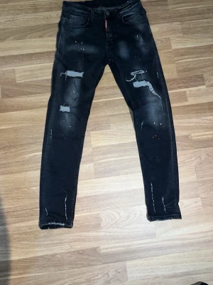 Svarta Dsquared2 jeans  - Snygga svarta dsquared2 jeans med slitna detaljer och färgstänk på framsidan. Jeansen har klassisk femficksdesign och smal passform. Perfekta för en trendig och avslappnad streetwear-look. Med strl 42 W30. Pris kan diskuteras och svarar snabbt