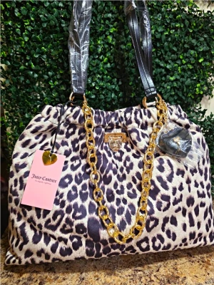 Leopardmönstrad handväska Juicy Couture - Snygg handväska från Juicy Couture med leopardmönster i beige och svart. Väskan har svarta handtag, en dekorativ guldfärgad kedja och detaljer i guld. Tillverkad i mjukt tygmaterial och har en klassisk, rymlig form. Perfekt för dig som gillar statement-accessoarer.