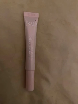 IsaDora Glossy Lip Treat rosa - Säljer ett IsaDora Glossy Lip Treat läppglans i en mjuk rosa nyans. Tuben är smidig och har en snedställd applikator för enkel applicering. Ger glans och återfuktar läpparna. Perfekt att ha i väskan för en fräsch look.