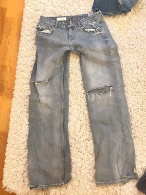 Zara jeans lågmidjde Ljusblå slitna raka jeans - Gråblåa. Säljer ett par ljusblå jeans med raka ben och flera slitningar och hål på både fram- och baksida. Jeansen har klassisk femficksmodell och en avslappnad passform. Perfekta för en trendig och avslappnad stil.