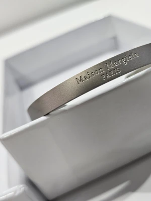 Maison Margiela silverfärgat armband - Snyggt och stilrent armband från Maison Margiela i matt silverfärgad metall. Armbandet har en minimalistisk design med Maison Margiela Paris ingraverat på ovansidan. Perfekt accessoar för dig som gillar exklusiva detaljer.
