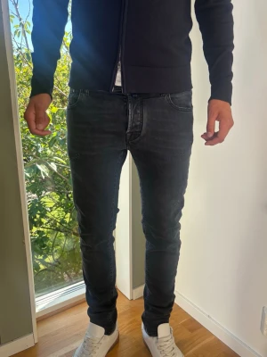 Jacob Cohën Nick Slim Jeans Herr   - Jacob Cohën i modellen Nick Slim. Mörkgrå/Svart nyans i mjuk modal- och bomullsmix med stretch som gör jeansen riktigt sköna på. Exklusiva detaljer Storlek: 34. Skick: Grade A/B (inga defekter och lite användning) Mått [platt]: (Jämför med en jeans som du gillar) A: Midja: 42 cm B: Längd: 107 cm C: Benslut: 16 cm D: Lår: 24 cm Passar bra på modellen på bilden som är 189 cm lång.  Passar +-5 cm därifrån (dubbelkolla mått).  Tveka inte att höra av dig vid frågor eller funderingar. Skickas snabbt!