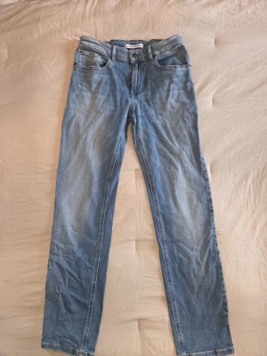Ljusblå raka jeans, storlek 14 - Säljer ett par ljusblå Calvin Klein jeans med rak passform och klassisk femficksdesign. Jeansen har normal midja och är tillverkade i ett mjukt denimtyg med lätt tvättad look. Perfekta för en avslappnad och trendig stil.