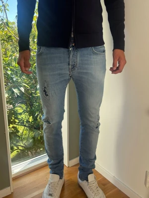 Jacob Cohën Nick Slim Jeans  - Exklusiva  jeans från Jacob Cohën (Nick Slim). Italiensk bomullsstretch, slitdetaljer. Skick: C Grade. Små röda fläckar som visas i bilderna men tycker själv de passar bra in i distressed känslan på jeansen. Patchen oxå lite sliten. Mått [platt]: A: Midja: 40 cm B: Längd: 105 cm C: Benslut: 15,5 cm D: Lår (från grenen): 24 cm Passar okej på modellen på bilden som är 189 cm lång. Passar kortare, från ca 183 cm & upp  (dubbelkolla mått). Tveka inte att höra av dig vid funderingar! Skickas snabbt! 