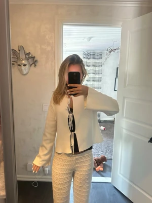 Vit tröja med knytband framtill - Trendig vit tröja med vida ärmar och dekorativa knytband framtill. Tröjan har en rak passform och är tillverkad i ett mjukt tyg som ger en avslappnad look. Perfekt för dig som gillar en unik och modern stil.